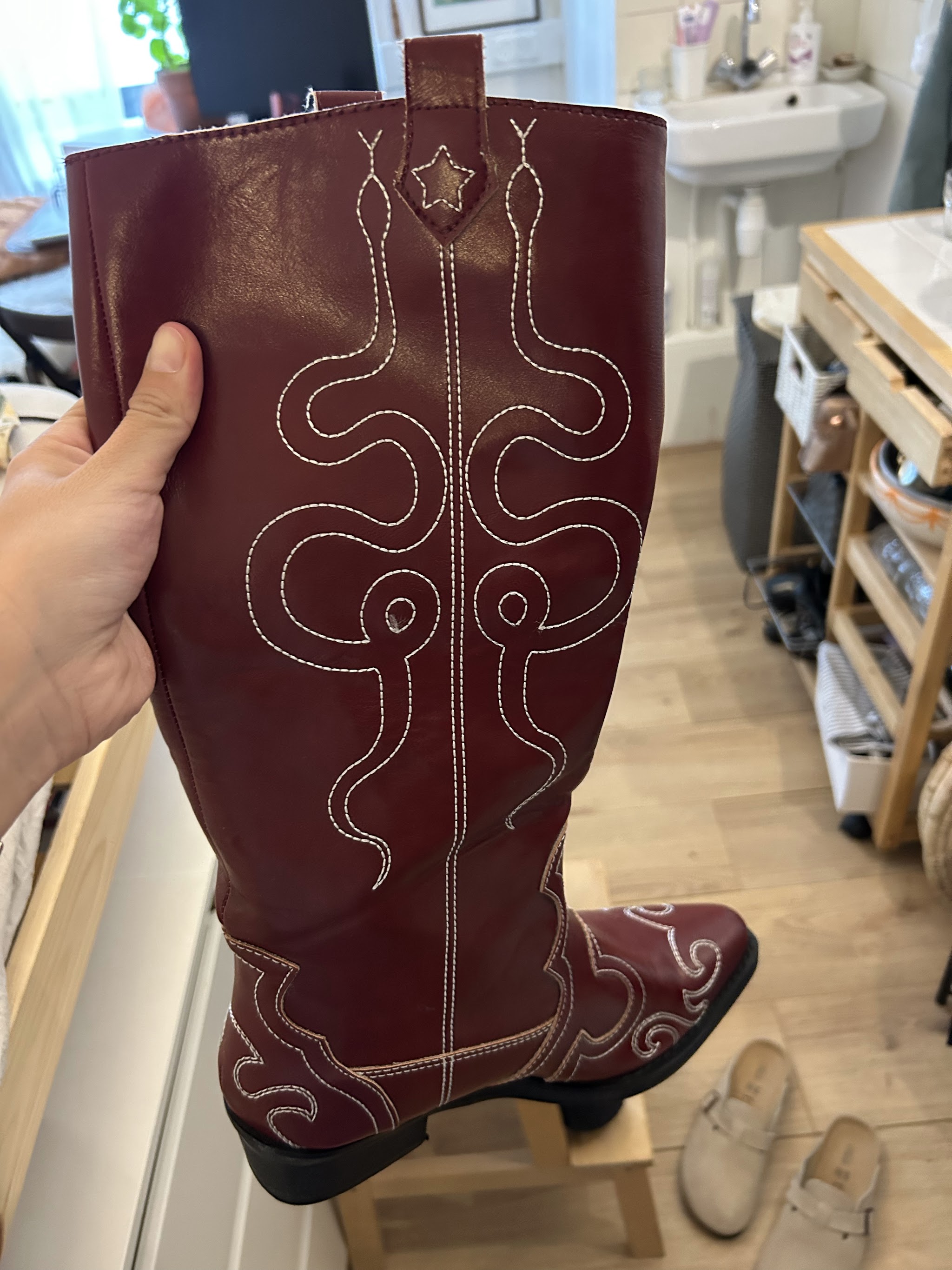 Een bordeauxrode cowboylaars met wit stiksel, omhoog gehouden in de werkplaats