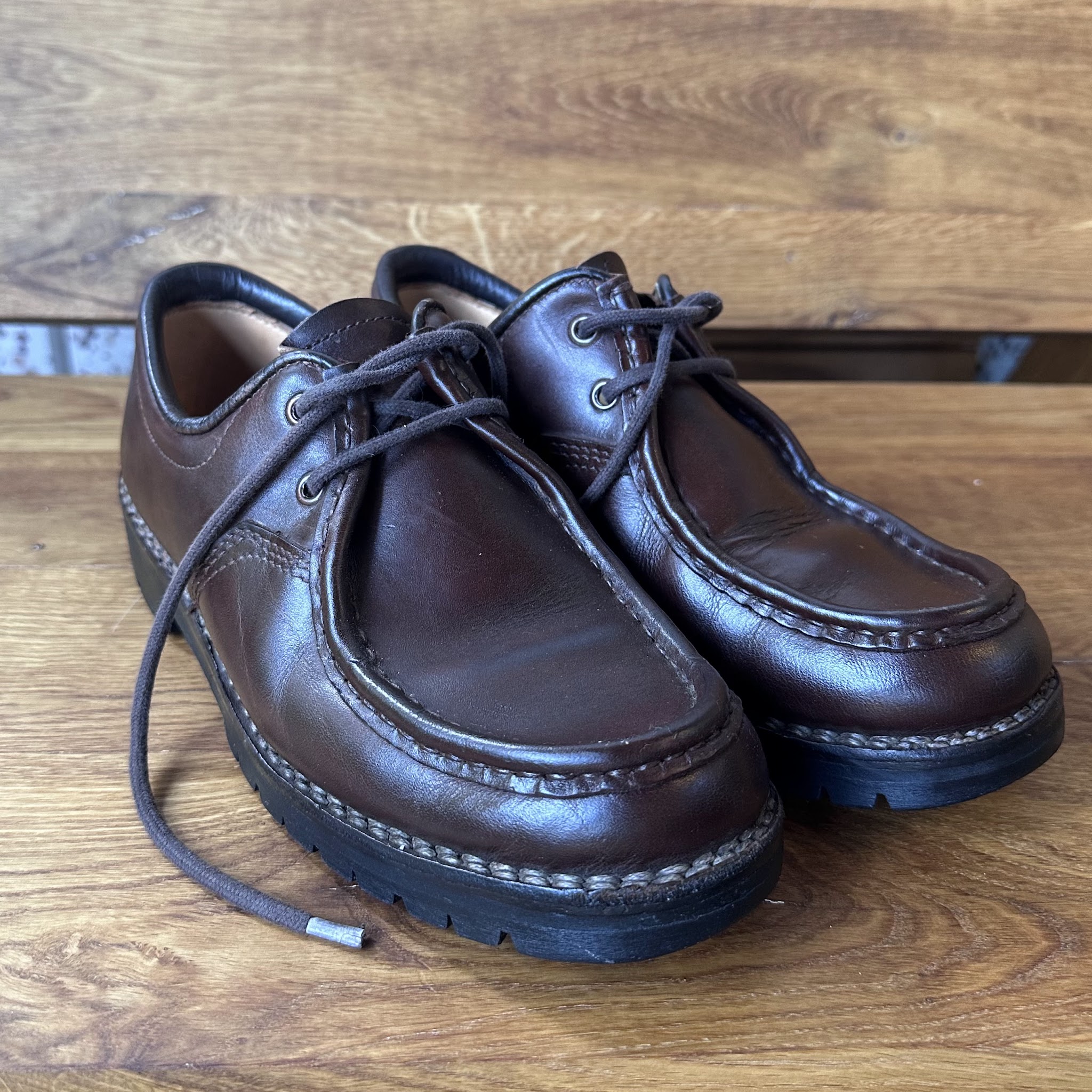 Een paar donkerbruine leren veterschoenen op een houten tafel na reparatie bij Het Slot